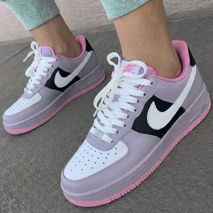 Nike Air Force sneakers with pink accents worn on a concrete surface