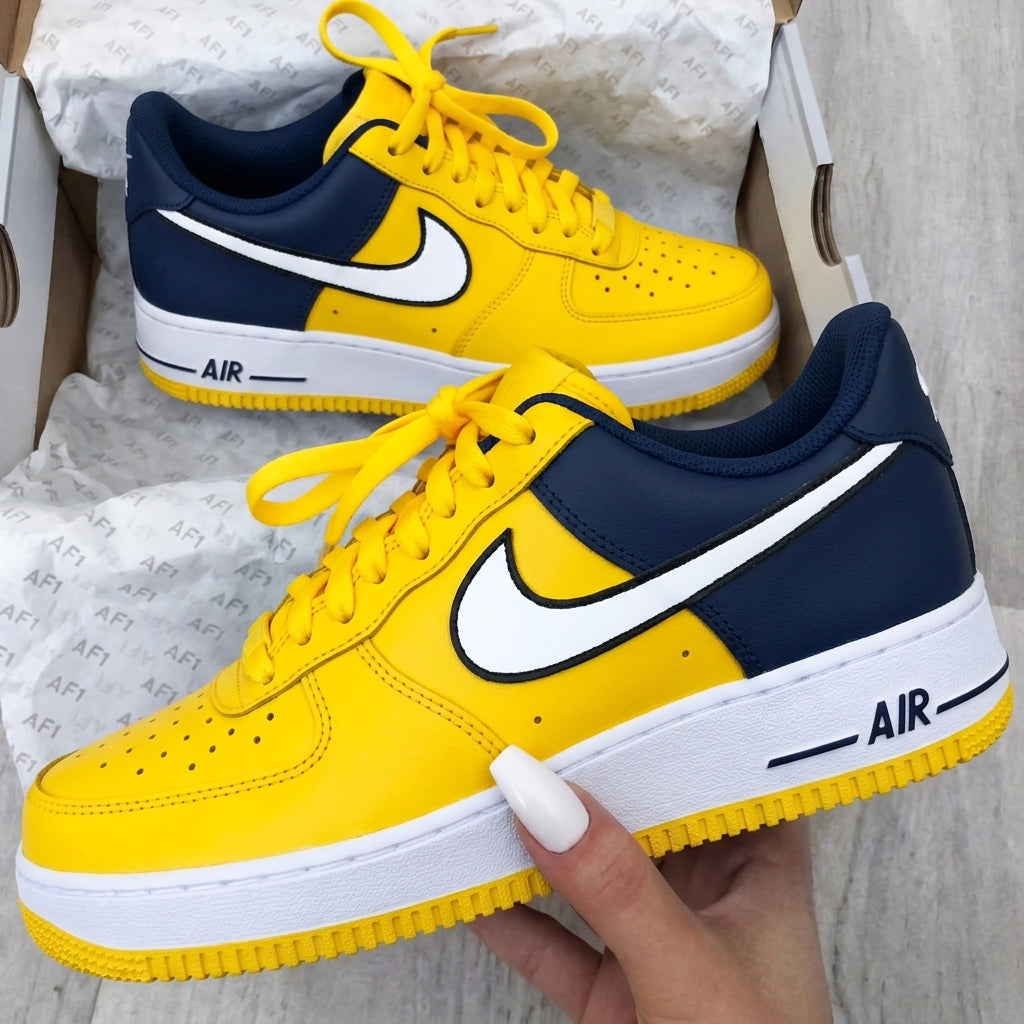 Yellow and navy Nike Air Force sneakers with a hand holding one shoe.